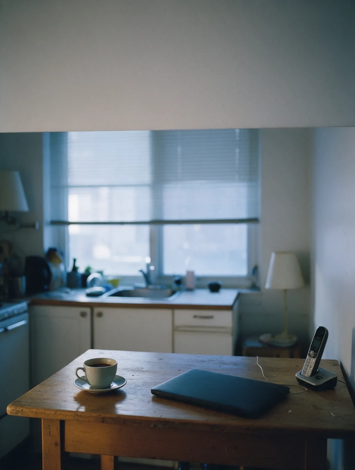 Un portable fermé sur une table de cuisine dans une lumière grise du matin, une tasse à côté.